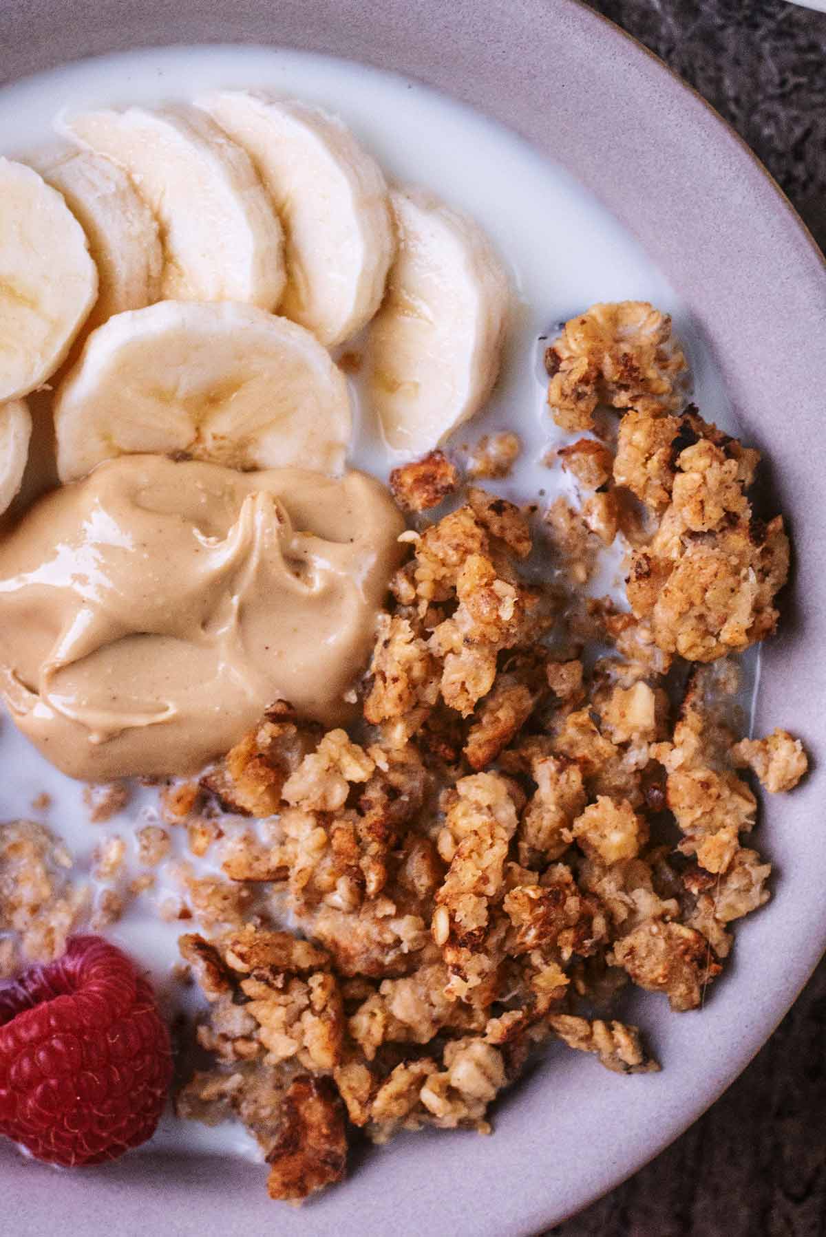 Clusters of scrambled oats with banana slices and some nut butter on top of thick yogurt.