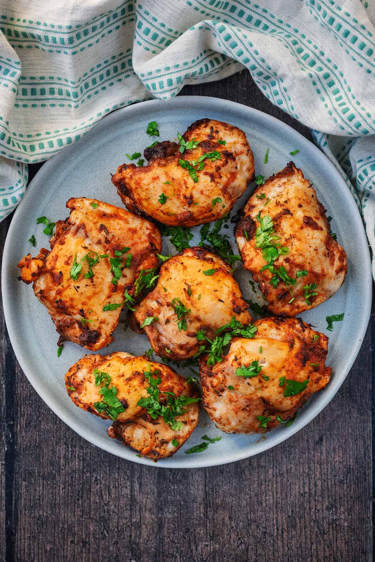 Six cooked chicken thighs on a plate next to a towel.