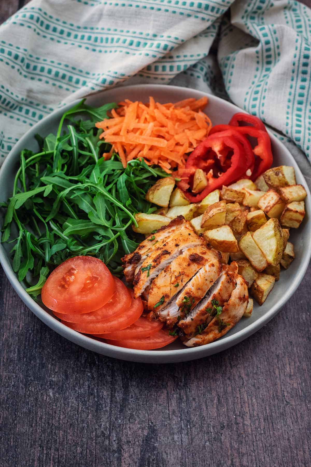 A bowl of salad and potato cubes with a cooked sliced chicken thigh.