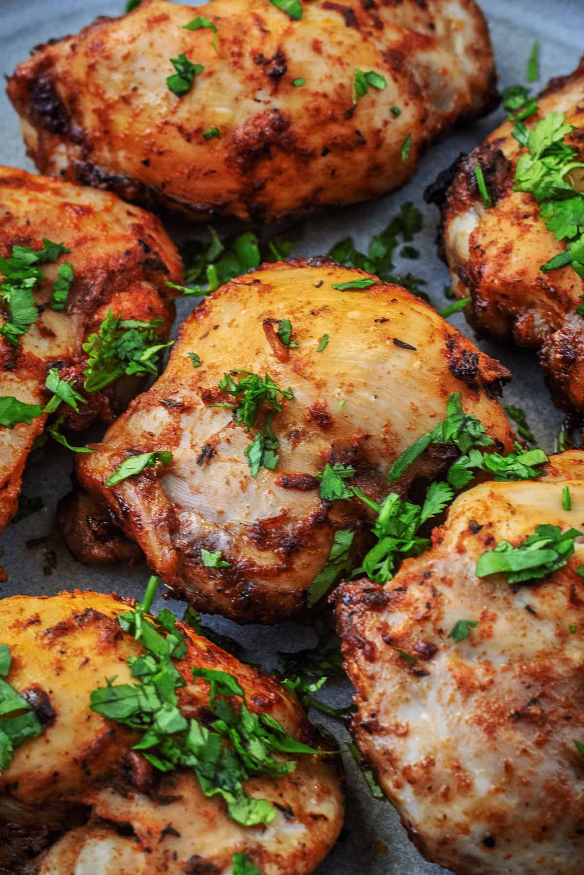 Cooked chicken thighs with chopped herbs scattered over them.