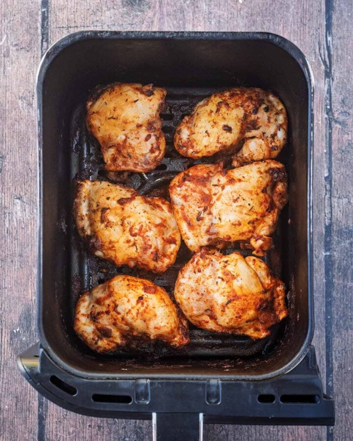 Cooked chicken thighs in an air fryer basket.