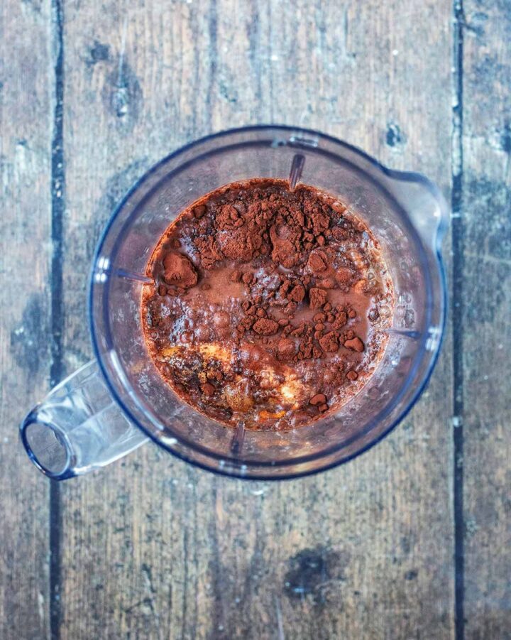 A blender jug containing, coffee, milk, banana and cocoa powder.