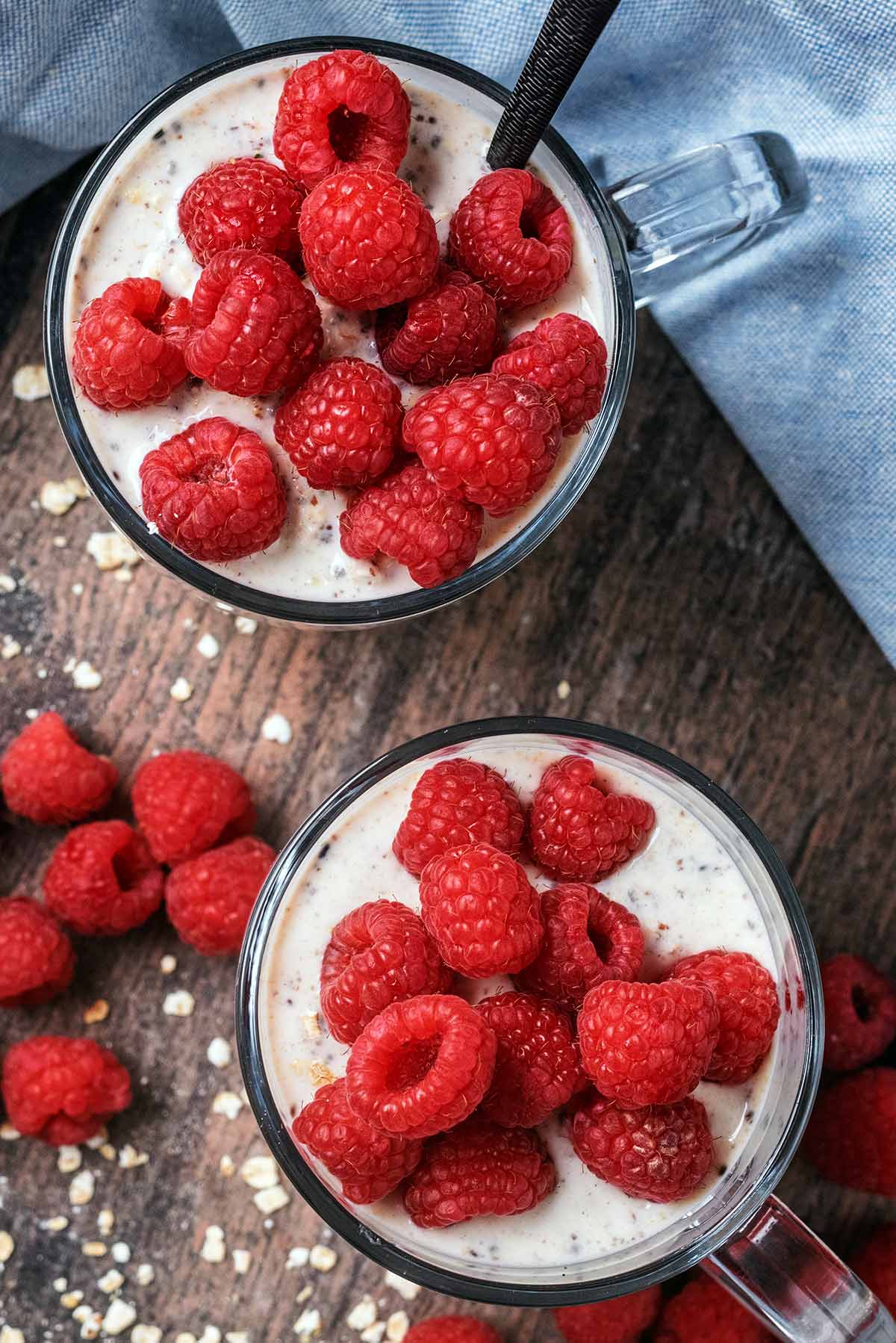 Two glasses of overnight oats topped with fresh raspberries, as viewed form above.