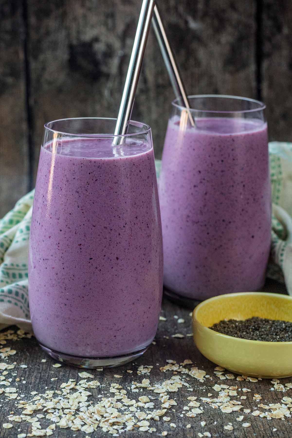 Two glasses of purple coloured smoothie, both with metal straws.