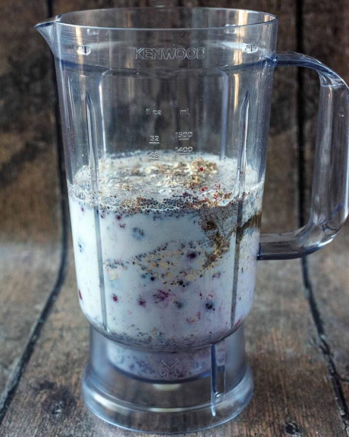 A blender jug containing milk, yogurt, berries and seeds.