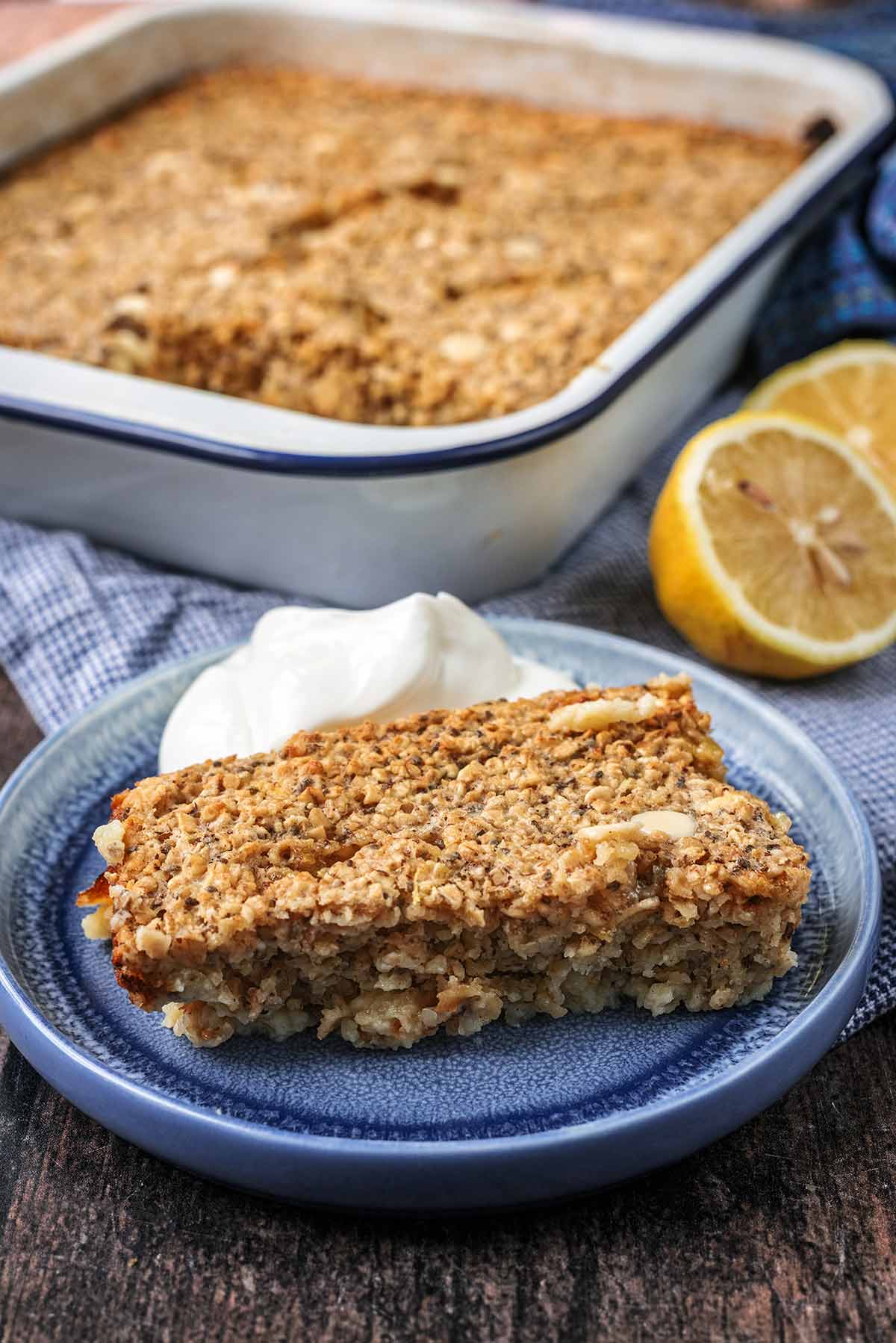 A portion of baked oats on a plate in front of the tray of baked oats it was removed from.