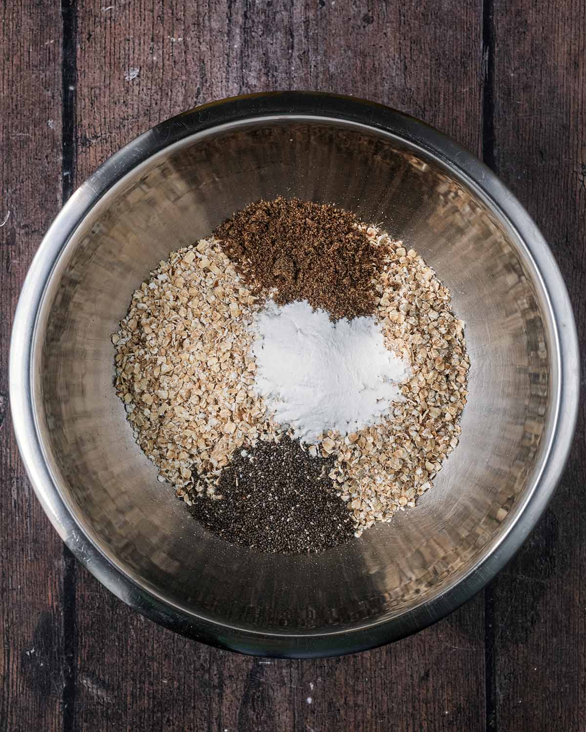 A mixing bowl containing oats, seeds and baking powder.