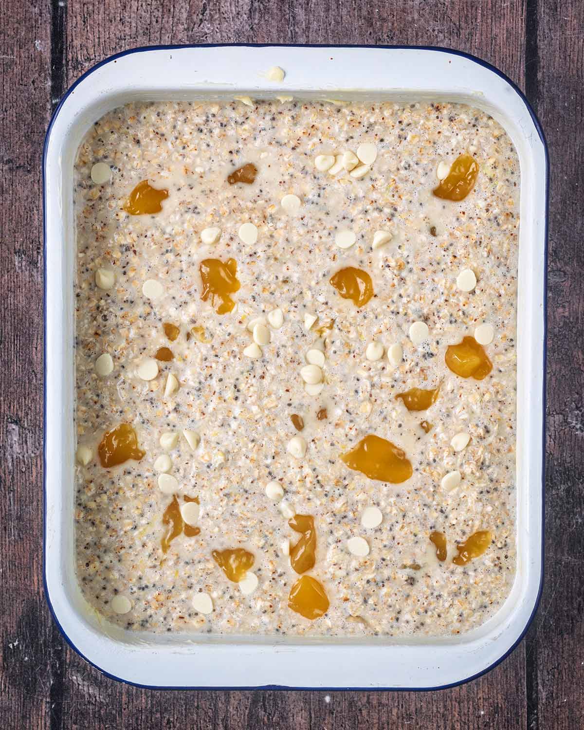The mixture in a rectangular baking dish. Dots of lemon curd and white chocolate chips on top.