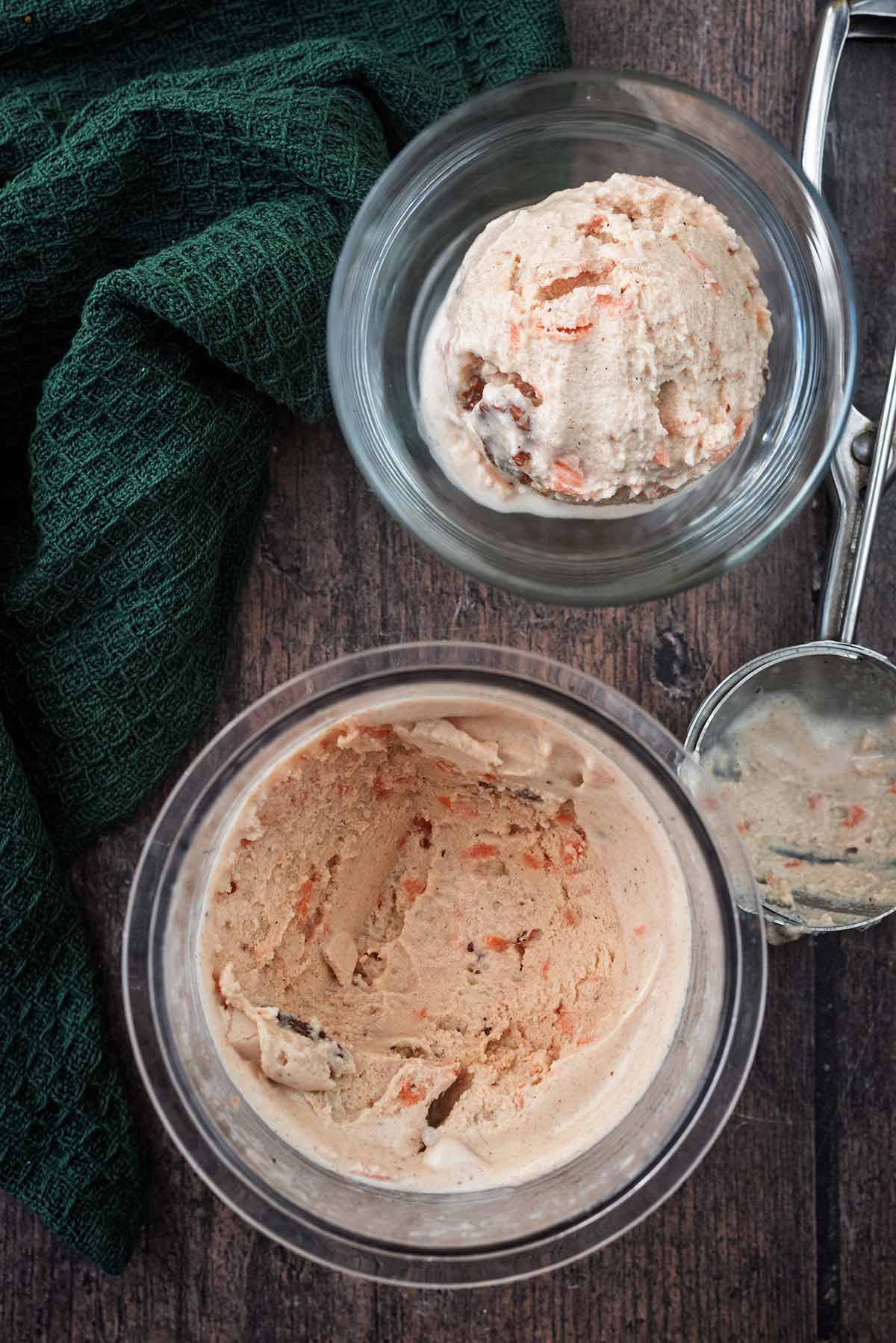 A tub of carrot cake ice cream with a portion in a serving glass next to it.