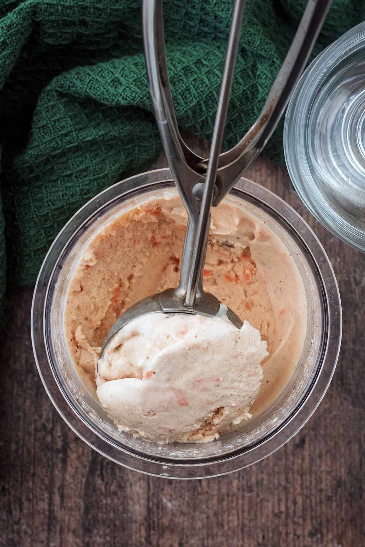 An ice cream scoop removing a portion of carrot cake ice cream from its tub.