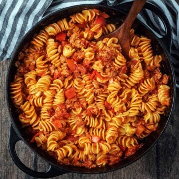 A large black pan full of sausage and pepper pasta.