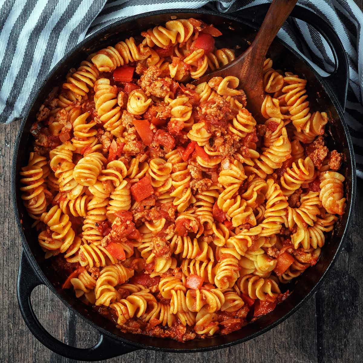 A large black pan full of sausage and pepper pasta.