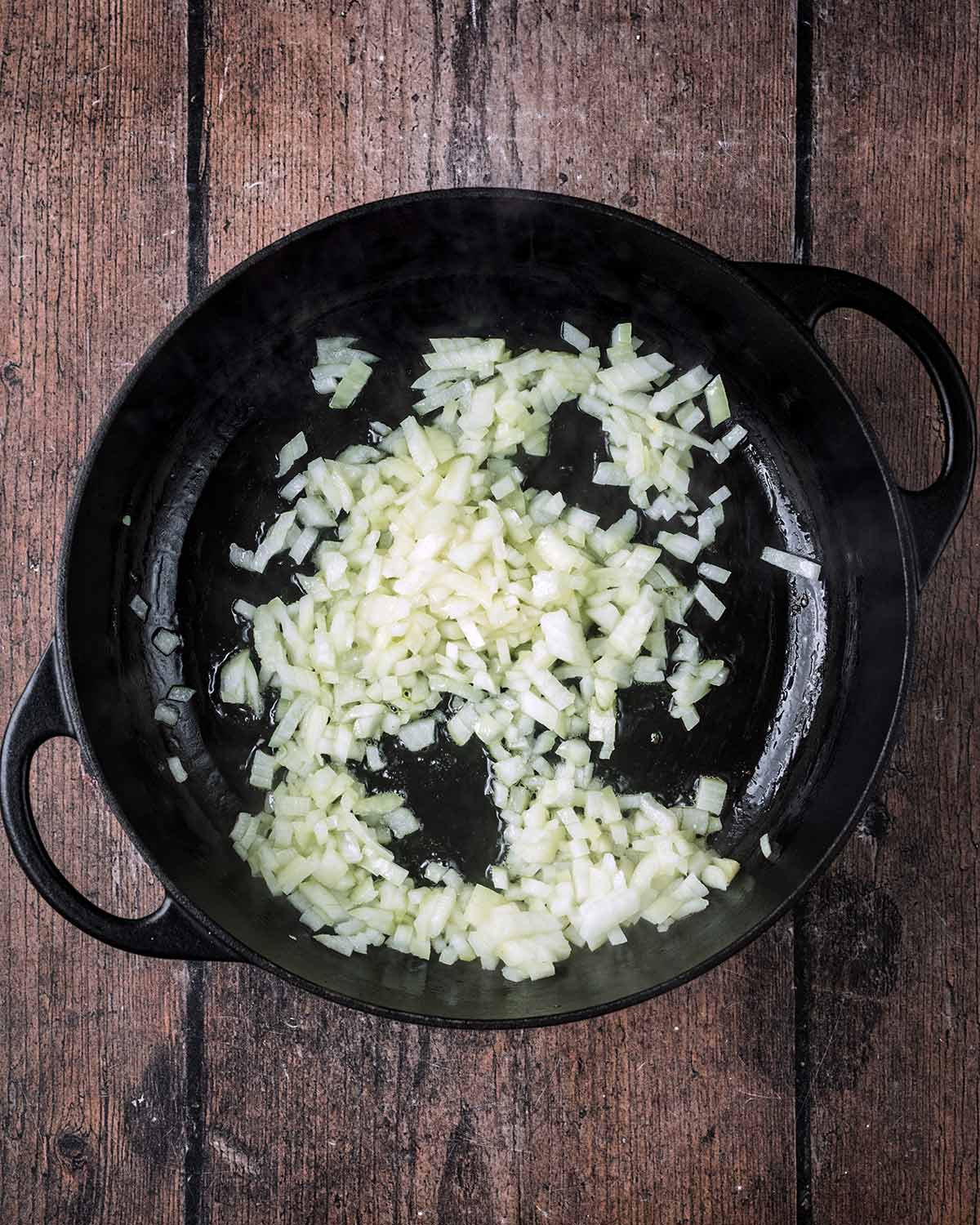 Chopped onion cooking in a large black pan.