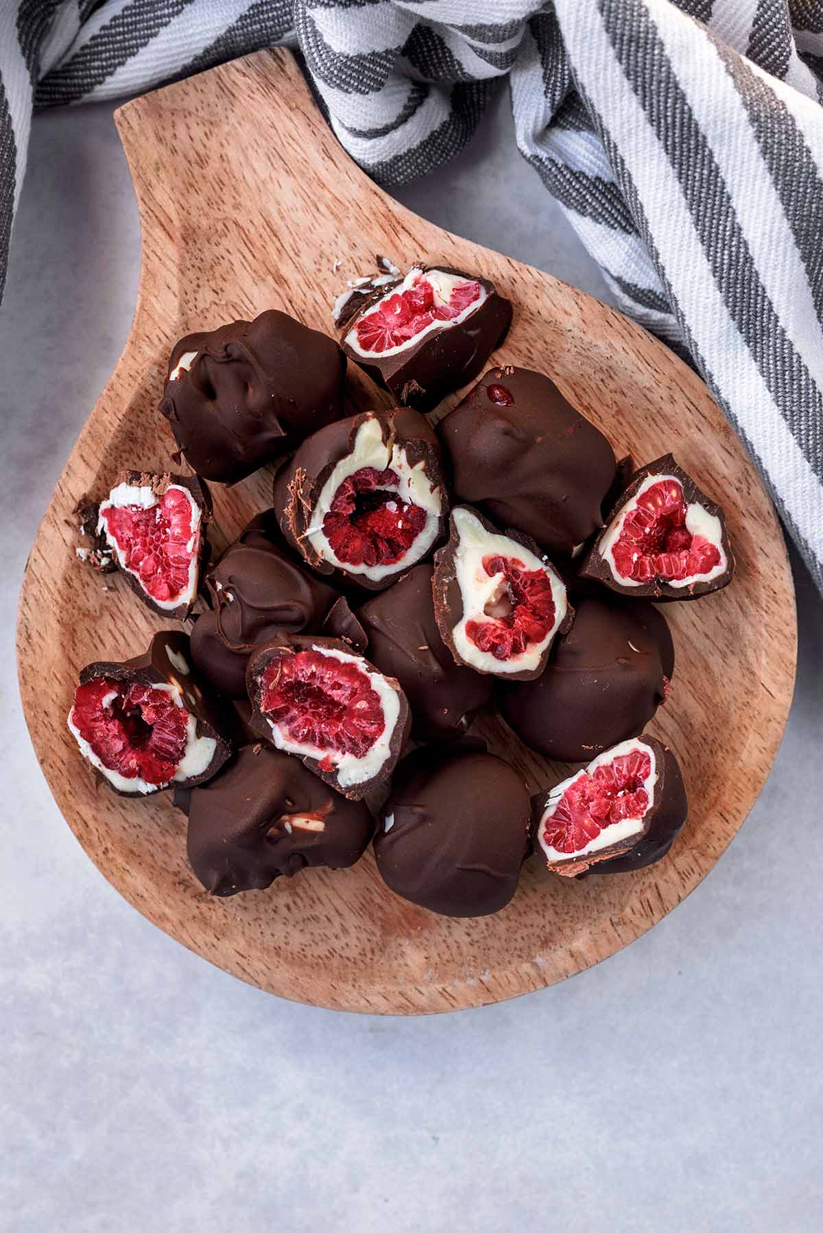 A selection of chocolte covered frozen raspberries on a small wooden board.
