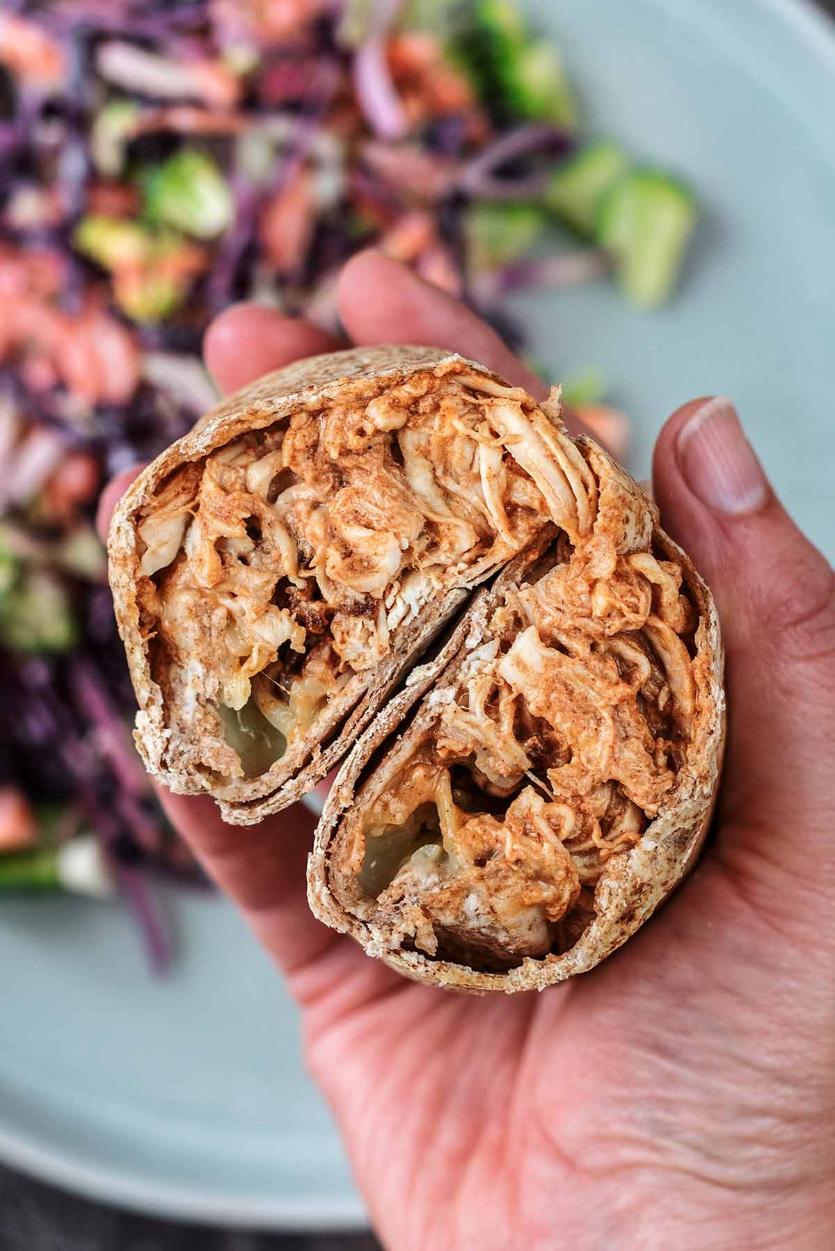 A hand holding two halves of a chicken wrap, showing the filling.