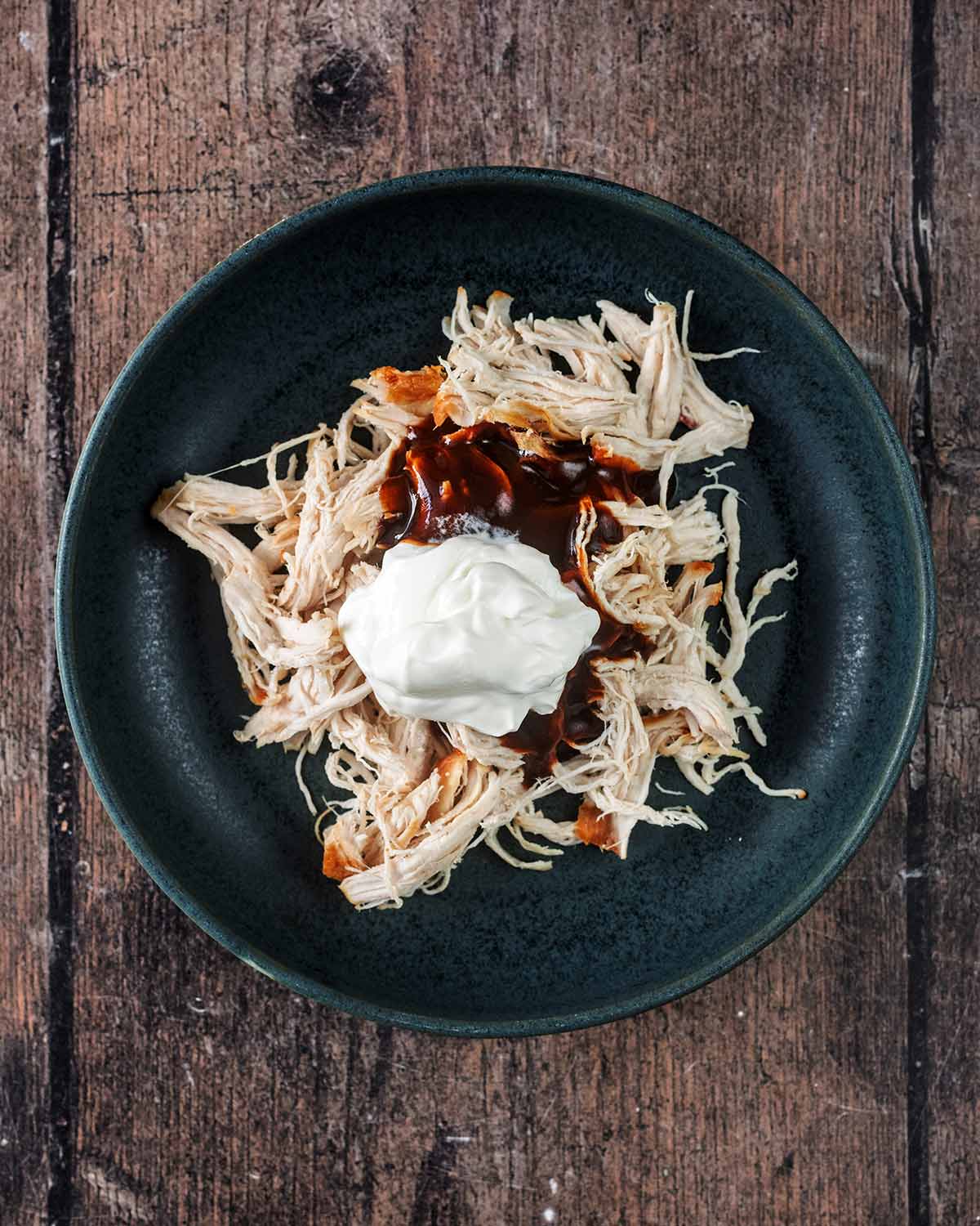 A bowl containing cooked, shredded chicken, yogurt and barbecue sauce.