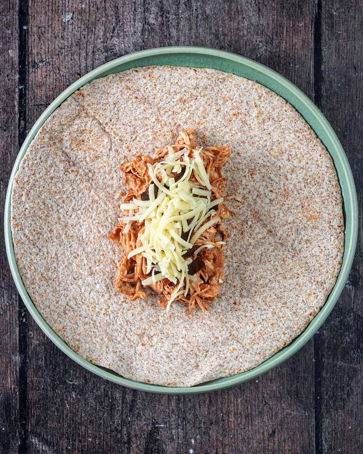 A large wholemeal wrap with the chicken mixture and grated cheese on it.