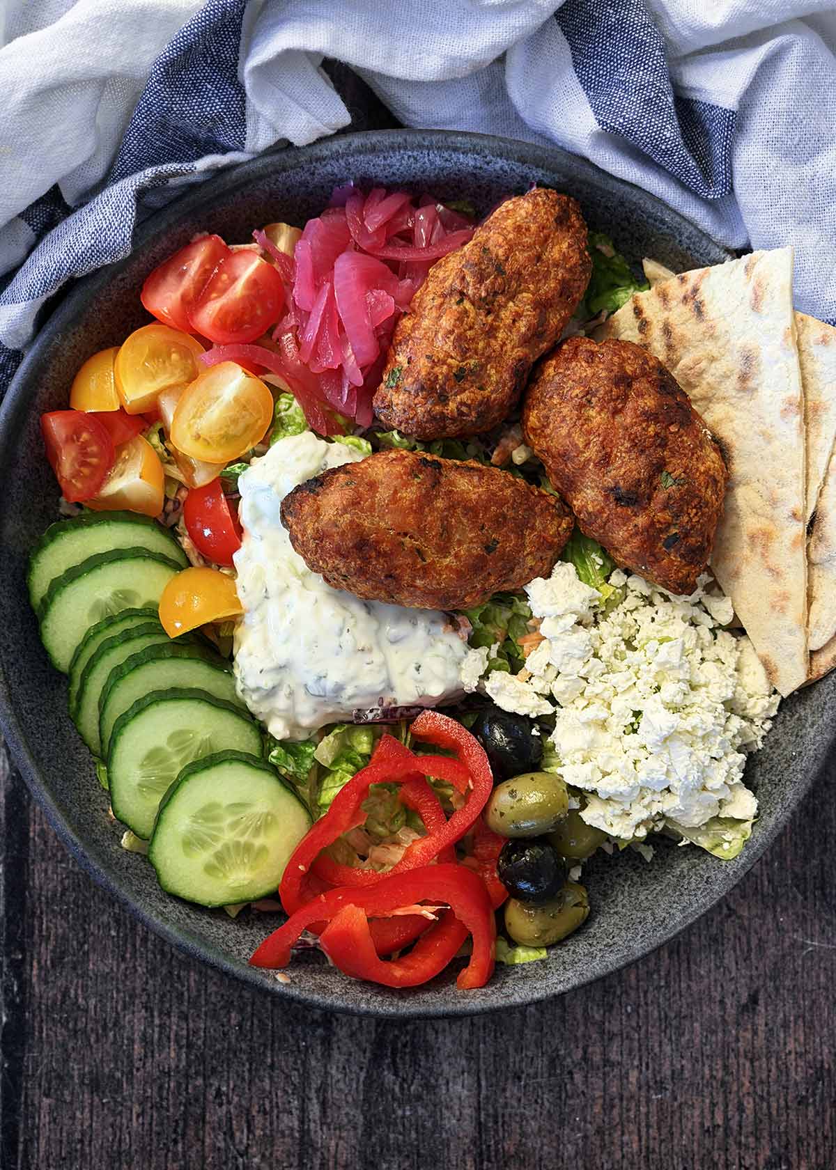 A bowl of various salad items, chicken koftas and flatbreads.