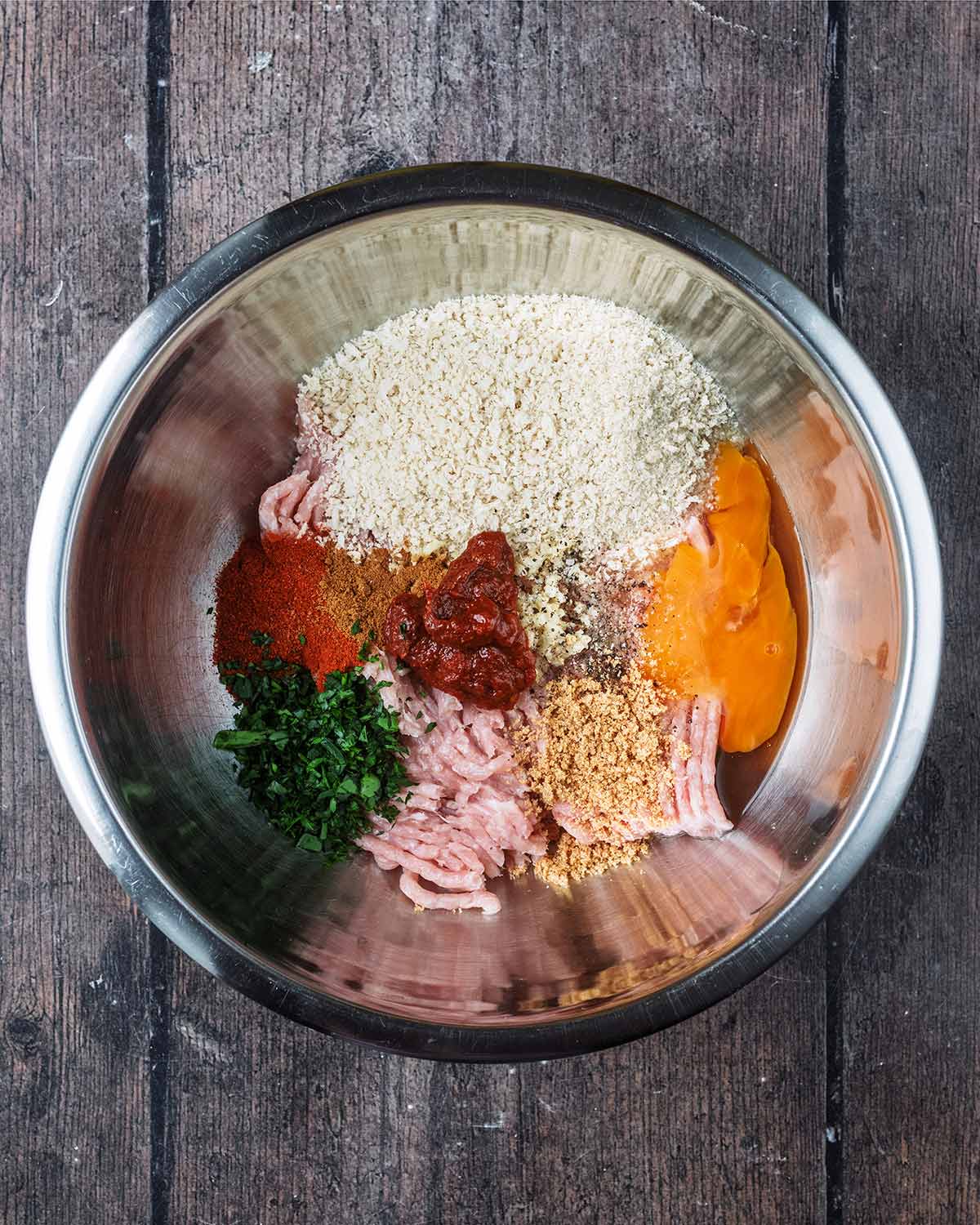 A mixing bowl containing minced chicken, egg, breadcrumbs, herbs and spices.