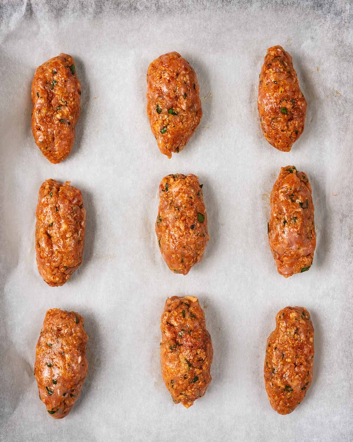 Nine uncooked koftas on a lined baking sheet.