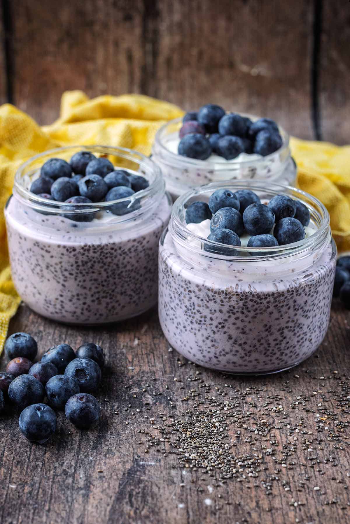 Three jars of chia pudding in front of a yellow towel.
