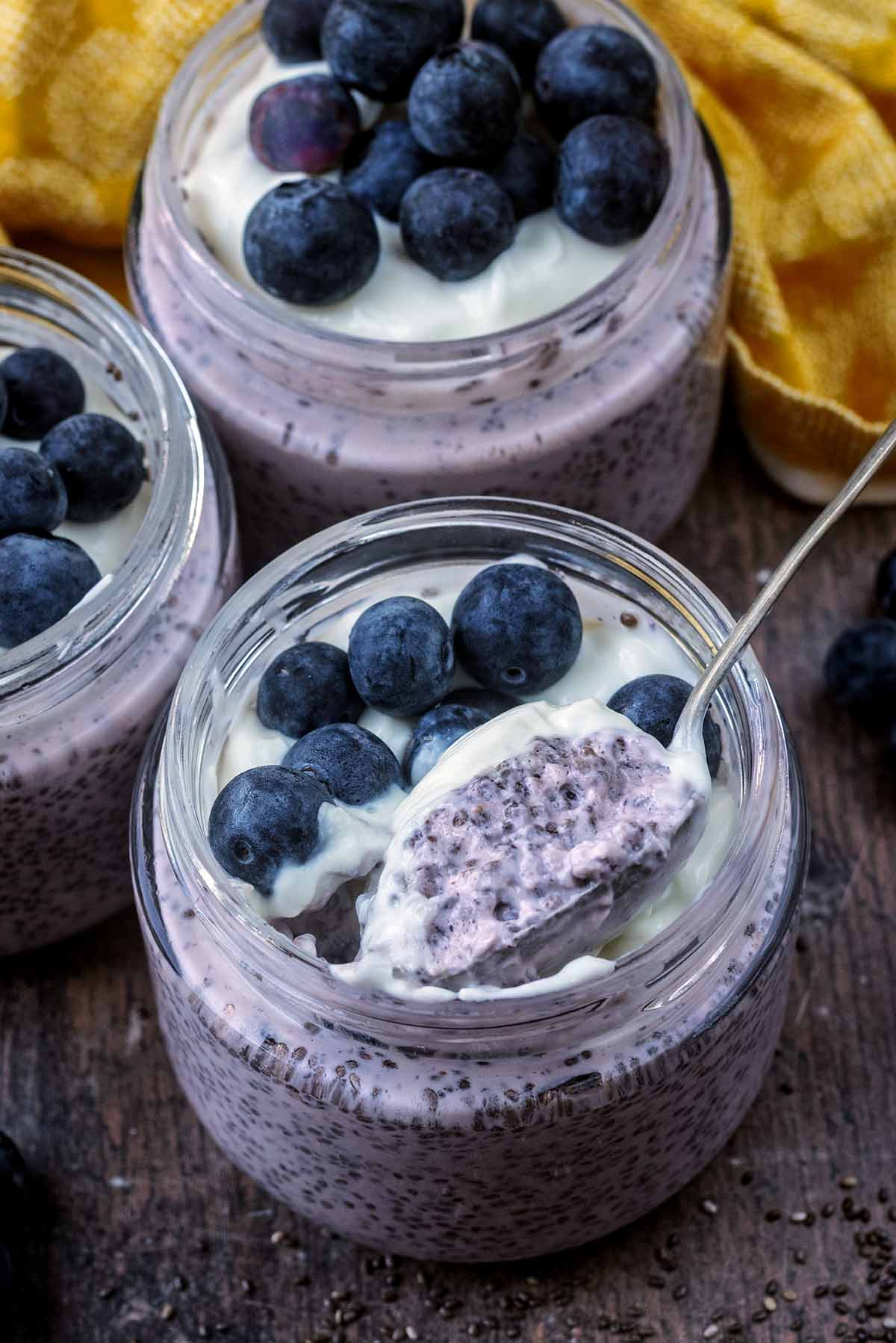 A jar of chia pudding, blueberries and yogurt with a small spoon in it.