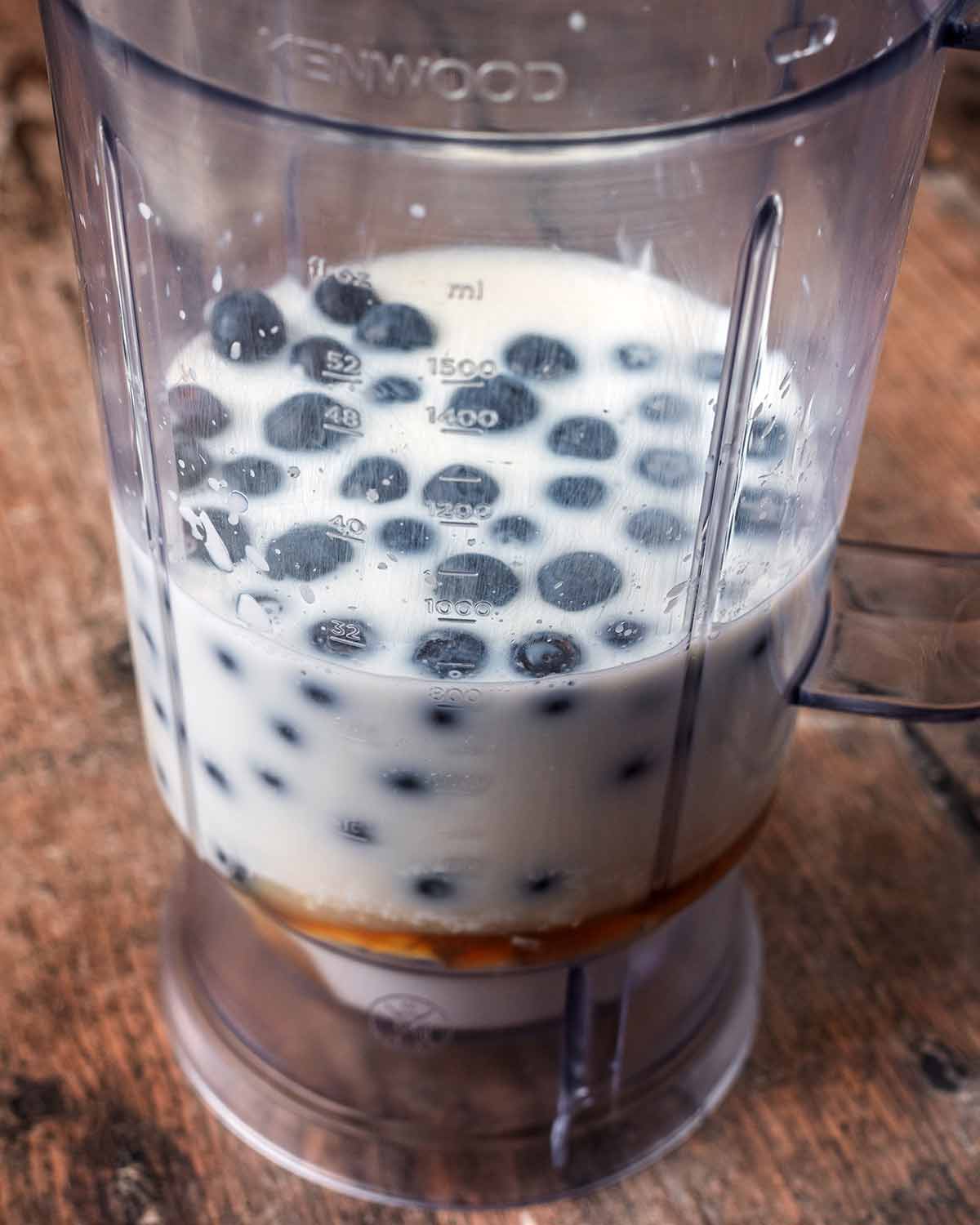 A blender jug containing yogurt, milk, blueberries, maple syrup and vanilla.