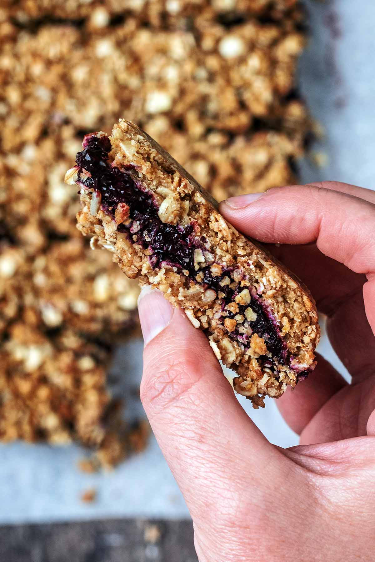 A hand holding an oat bar showing the layers of oats and jam filling.
