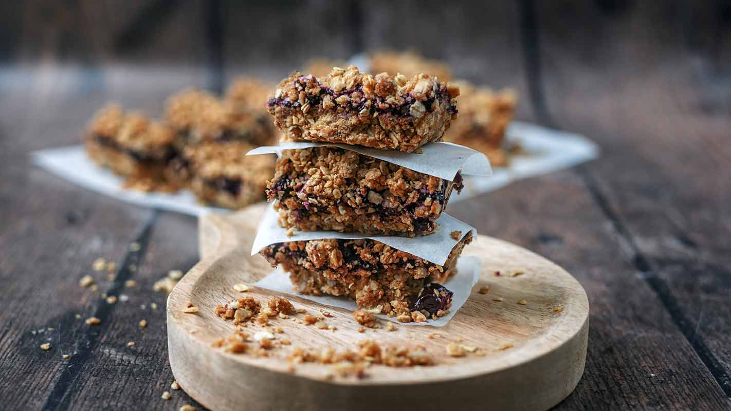 Three blueberry oat bars stacked up on a small wooden board.
