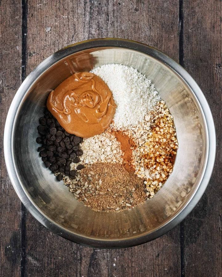 A large mixing bowl containing oats, desiccated coconut, seeds, chocolate chips and peanut butter.