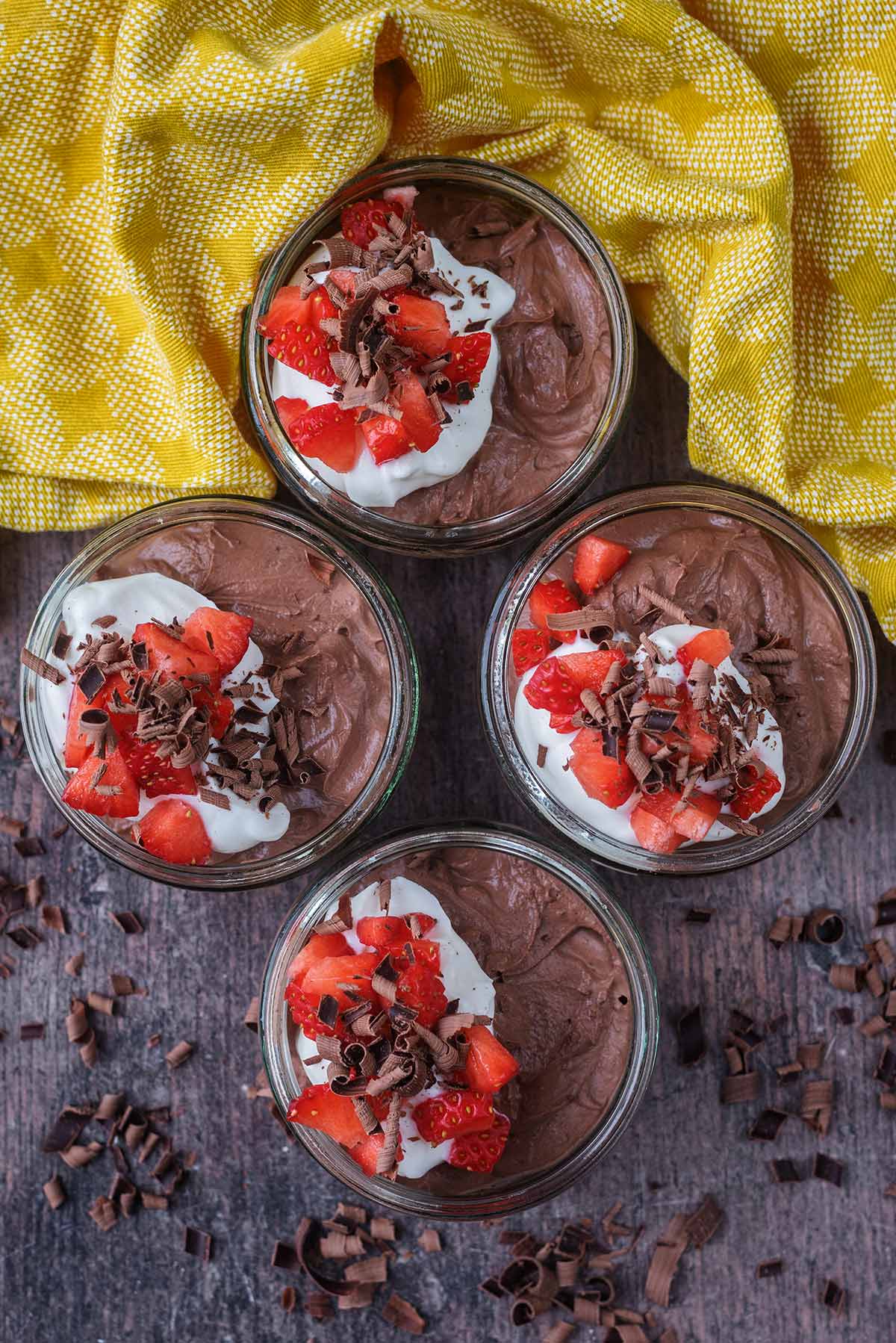Four serving glasses full of chocolate mousse next to a yellow towel.