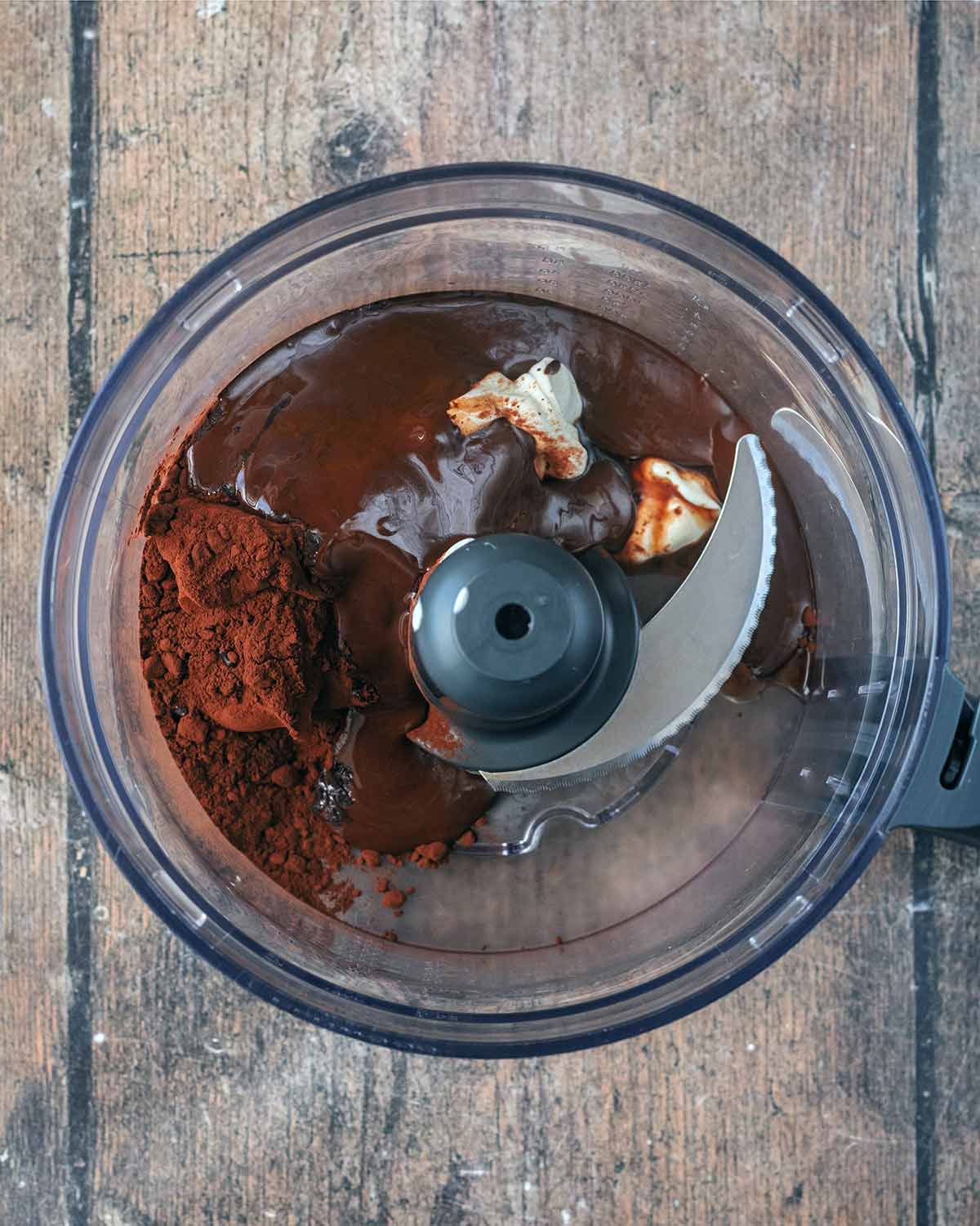 A food processor containing yogurt, melted chocolate, cocoa powder and vanilla.
