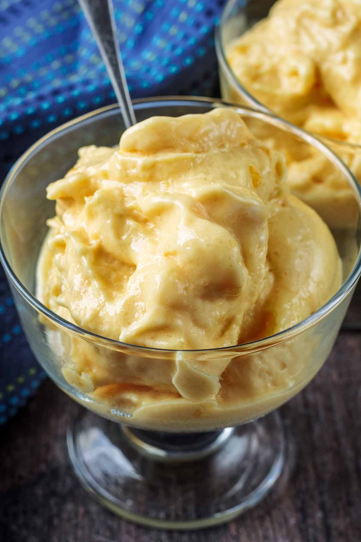 Yellow frozen yogurt in a glass with a spoon.