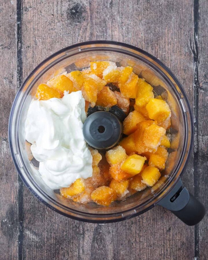 Chunks of frozen mango, yogurt and maple syrup in a food processor.
