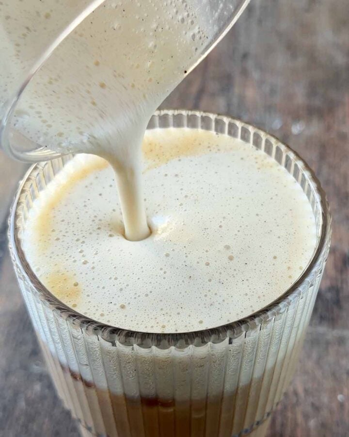 Foam being poured on top of a glass of iced coffee.