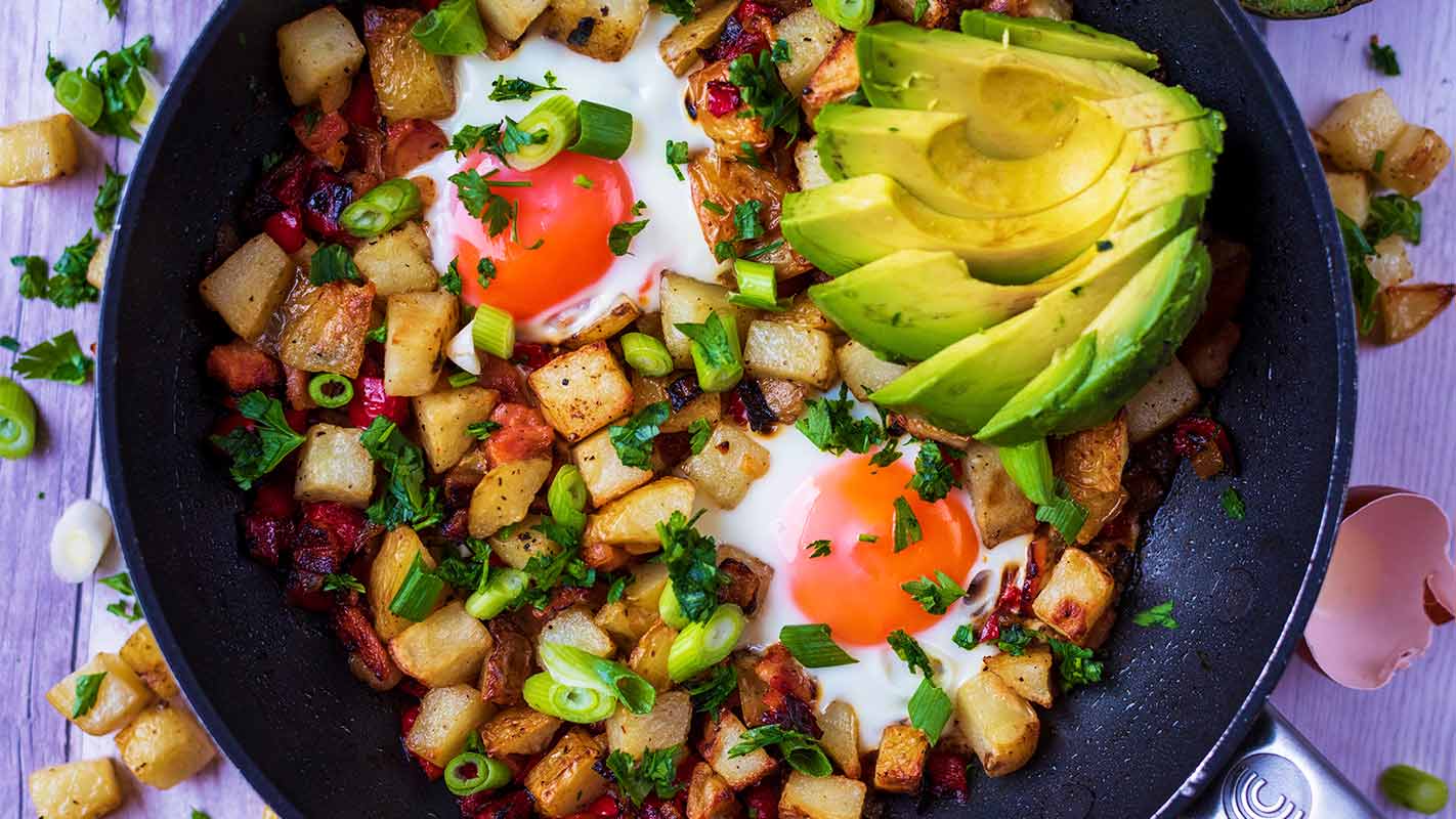 Breakfast Hash in a frying pan with sliced avocado.