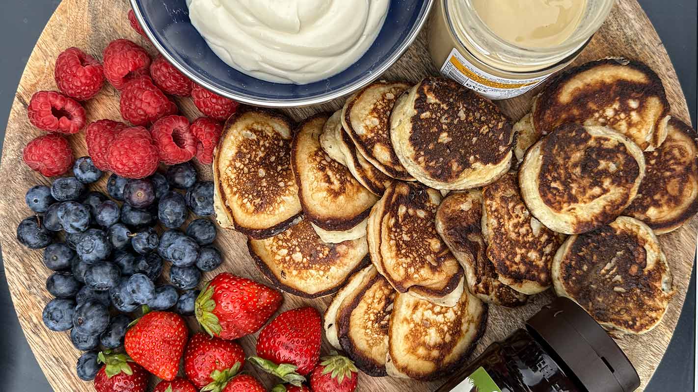 A wooden board with pancakes, berries, yogurt and nut butter.