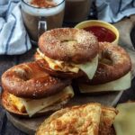 Three egg and cheese bagels stacked on a wooden board.