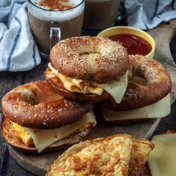 Three egg and cheese bagels stacked on a wooden board.