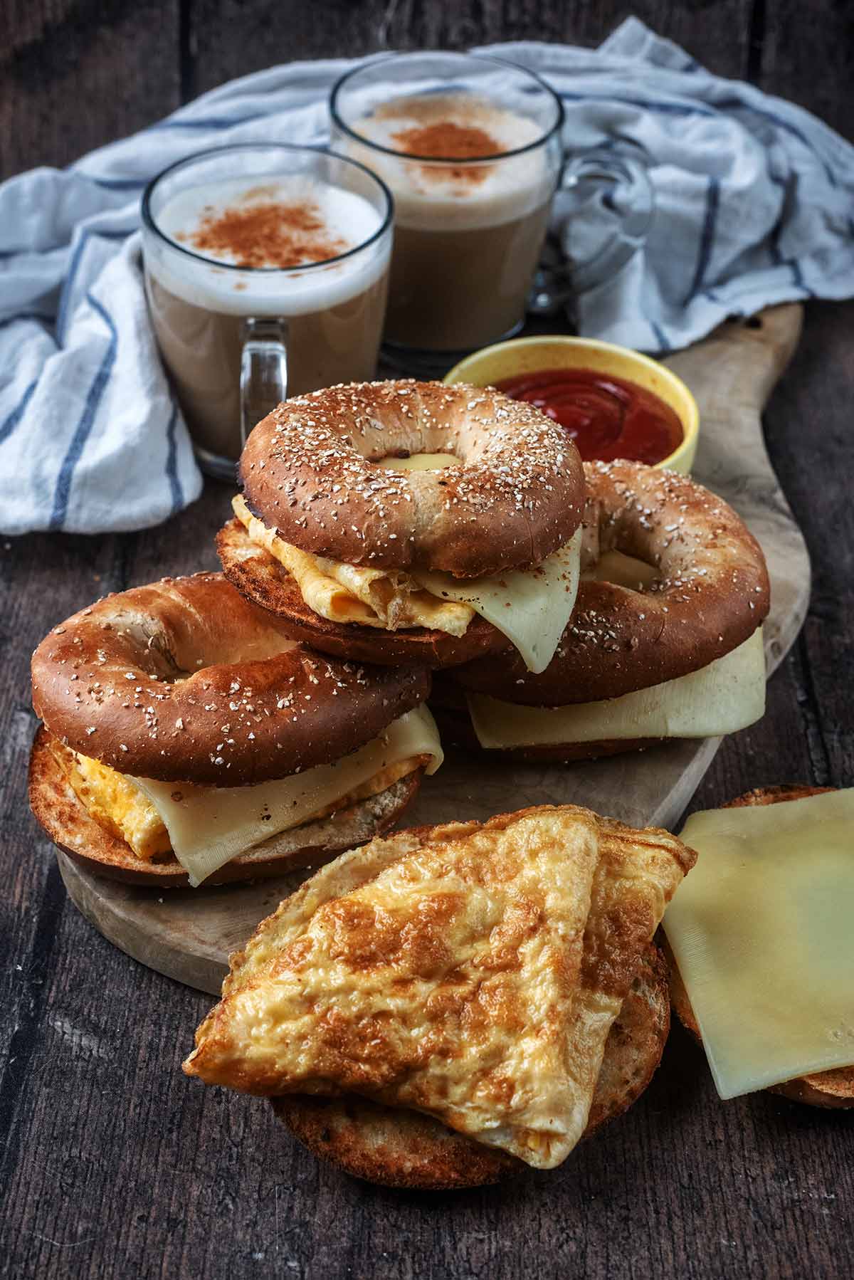 Three cheese and egg bagels behind another bagel that is opened.