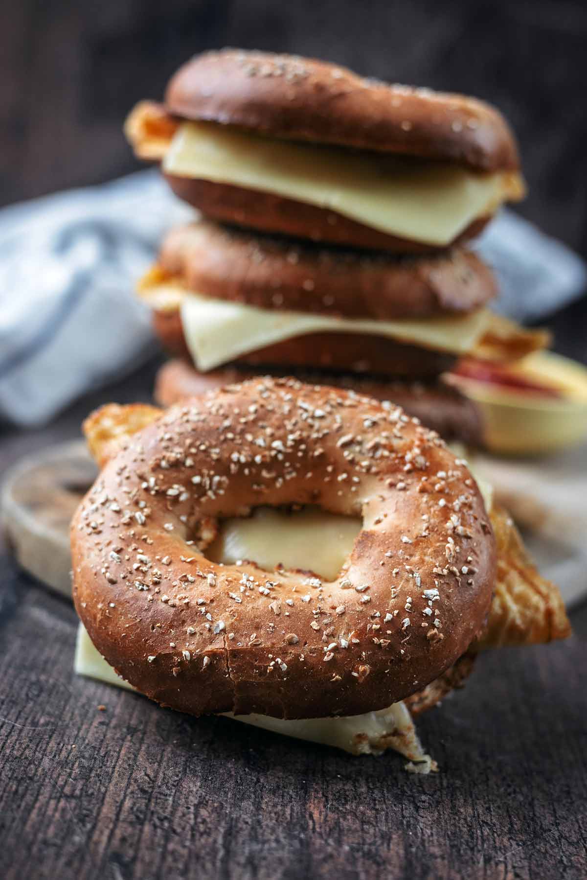 A tower of three bagels with another egg filled bagel in front of them.