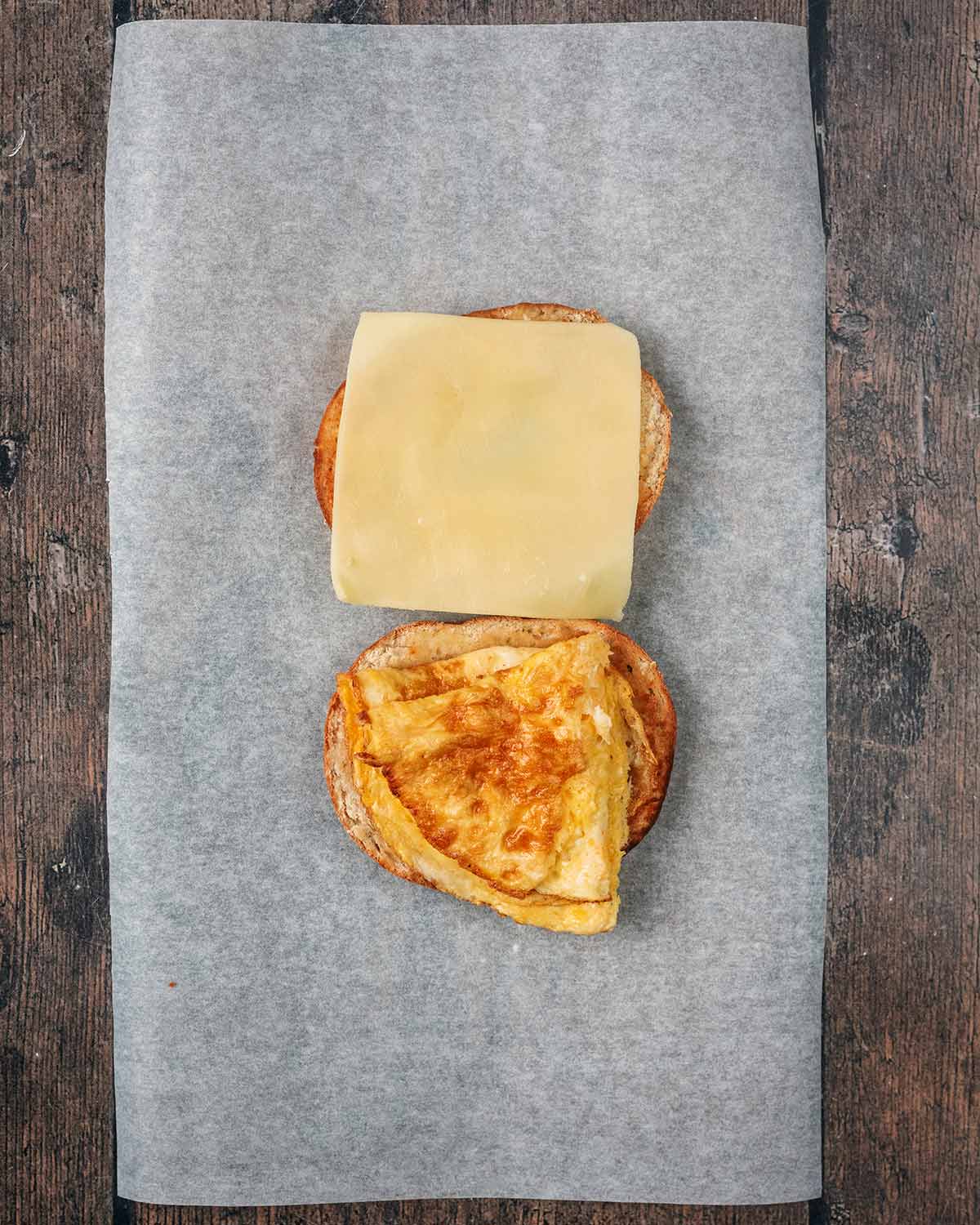 A cheese slice on one half of a bagel and a folded omelette on the other half.