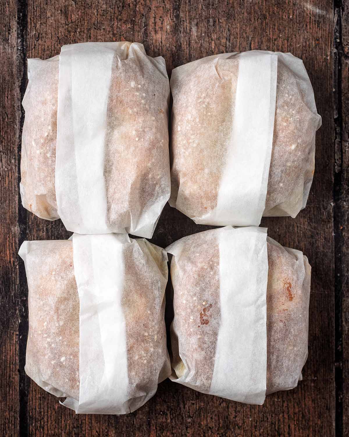 Four parchment paper wrapped bagels on a wooden surface.
