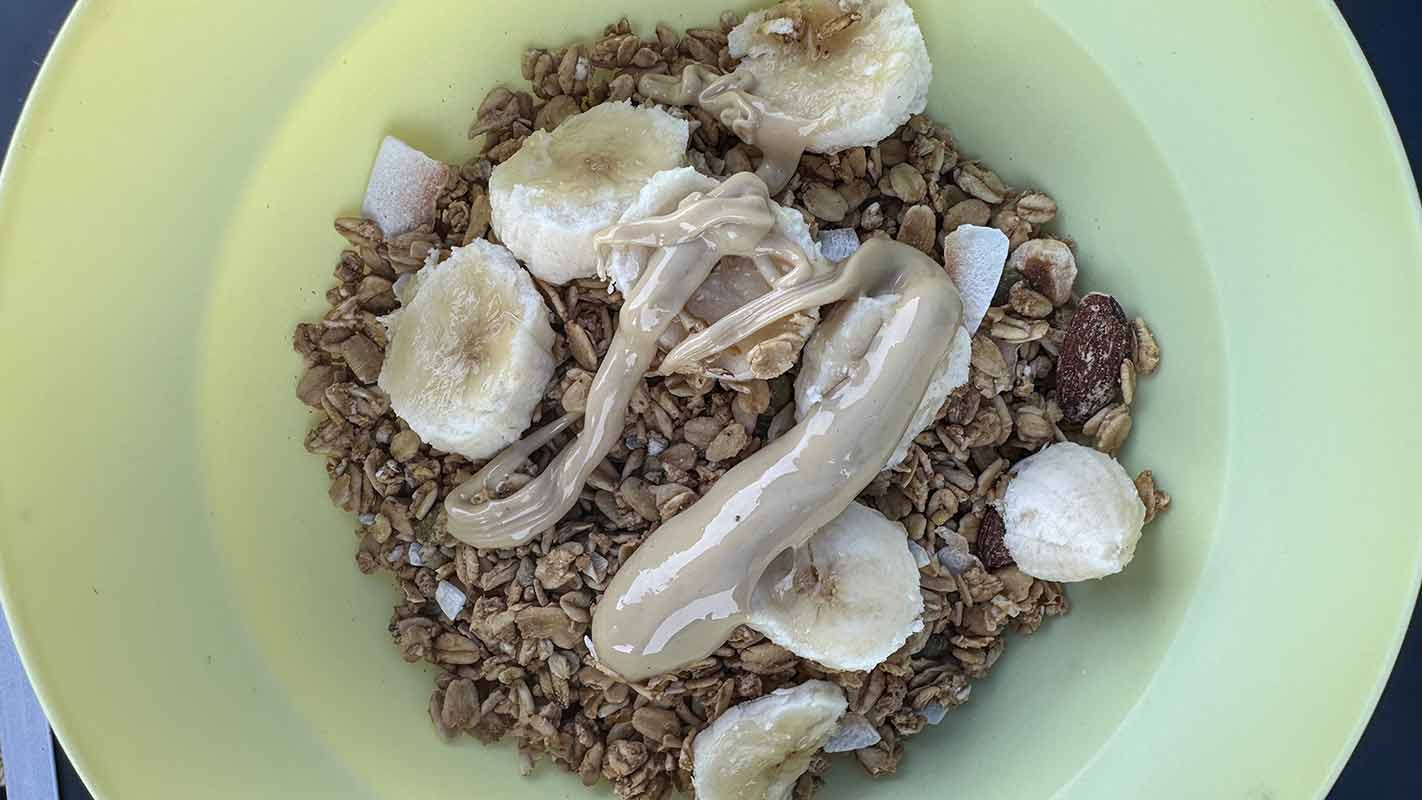 A plastic bowl full of granola, banana slices and nut butter.