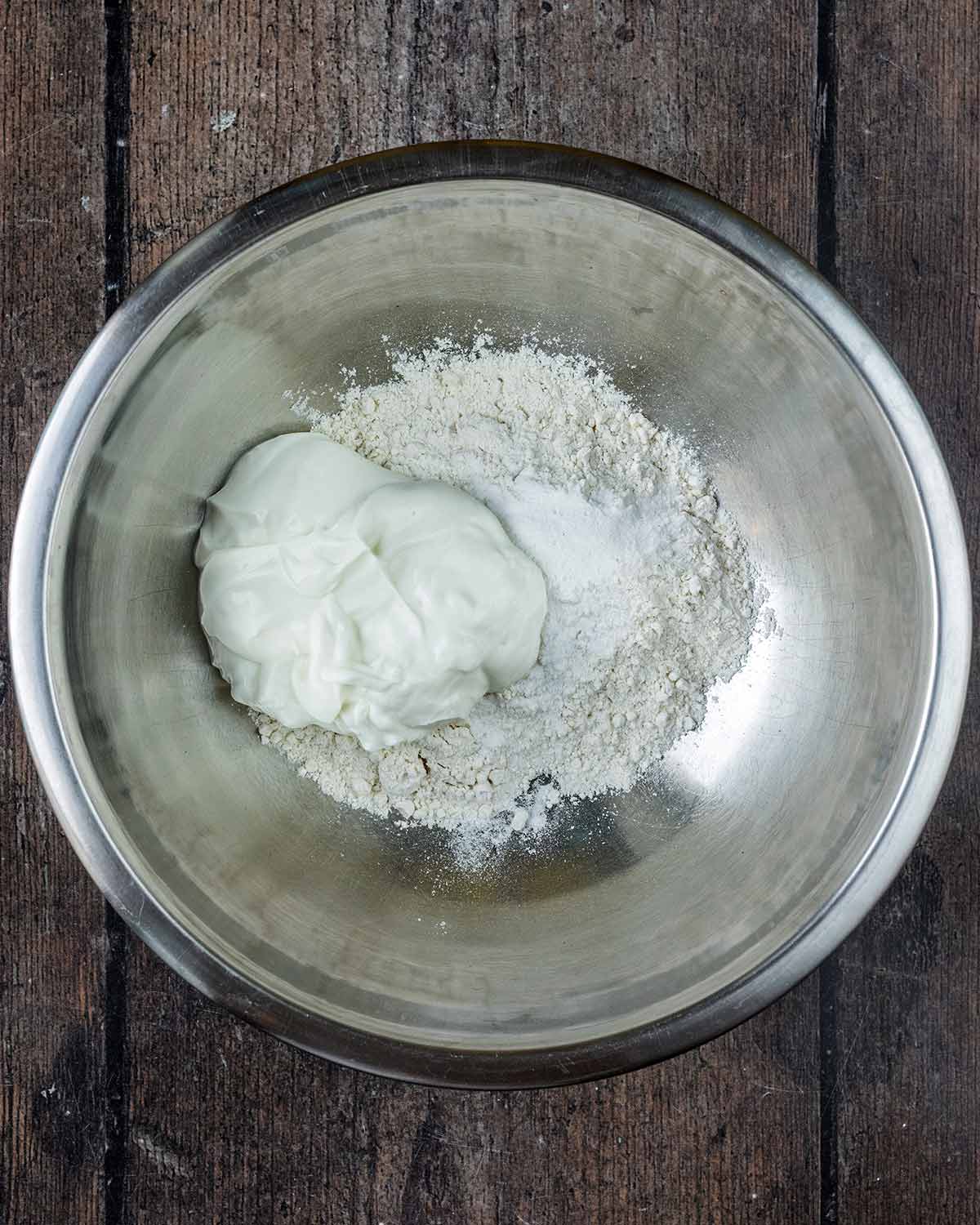 A mixing bowl containing flour, baking powder and yogurt.