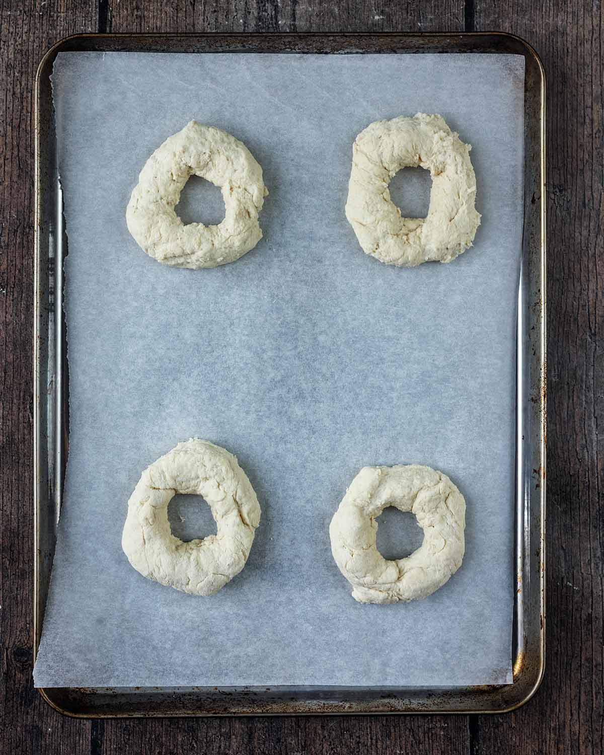 Four uncooked bagels on a lined baking sheet.