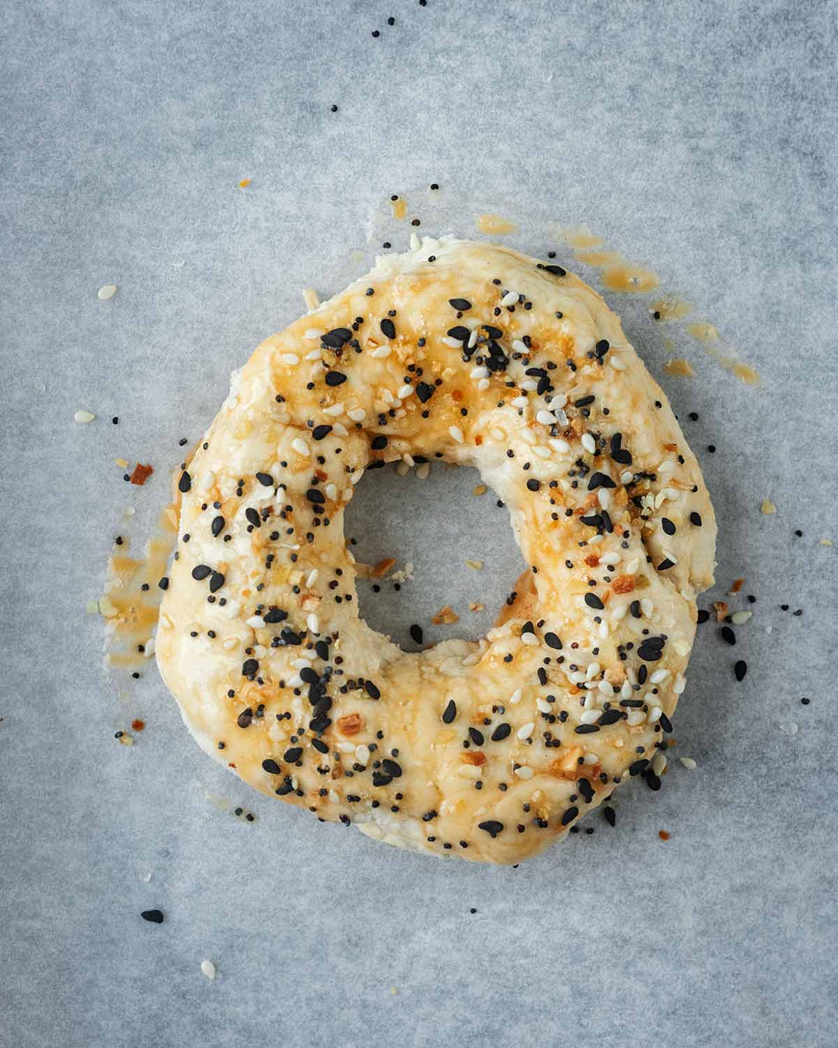 An uncooked bagels topped with an egg wash and mixed sesame seeds.