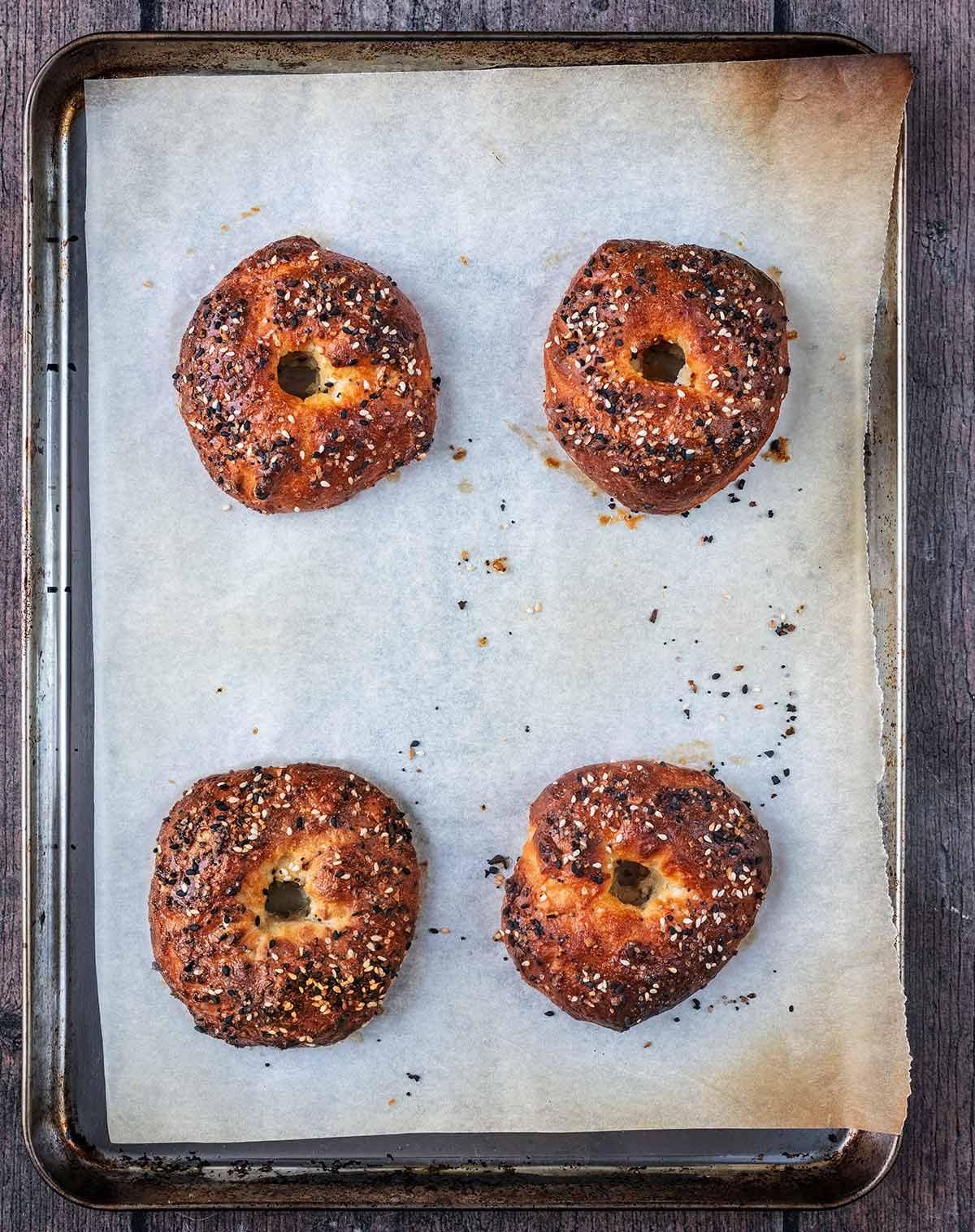 Four baked bagels on the baking tray.