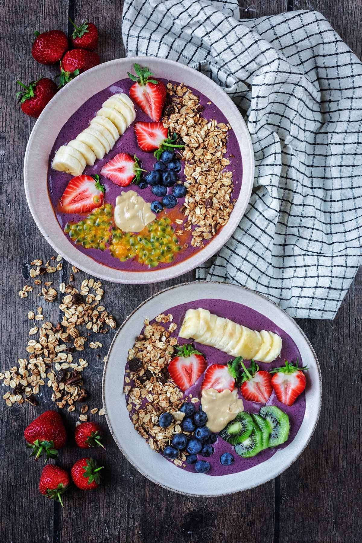 Two acai bowls next to a striped towel and some strawberries.