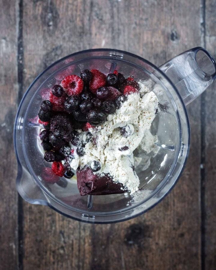 A blender jug containing frozen acai, frozen berries, yogurt and protein powder.